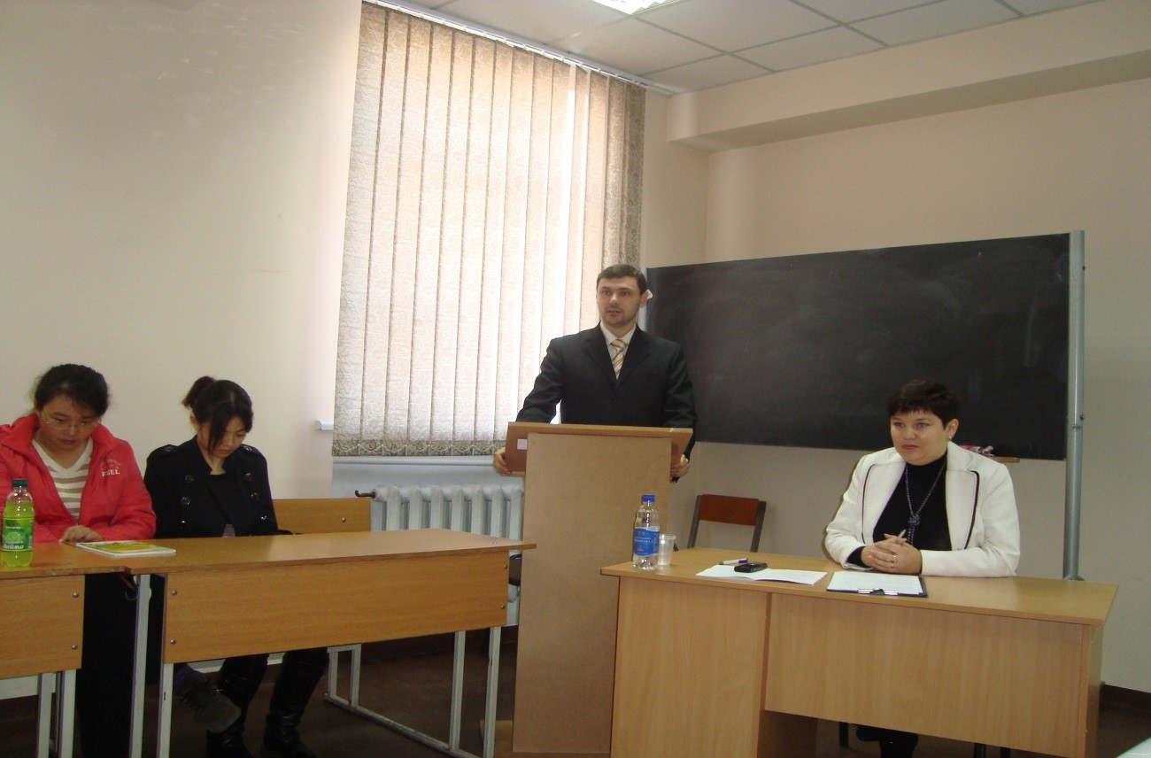 man speaking at pult, three women sitting right and left